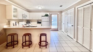 A kitchen with white cabinets, a central island with stools, a microwave, a toaster, and a refrigerator. - Spacious Townhome W/Garage-5 Minute Walk to BEACH! Community Pool, Enjoy! (Panama City Beach)
