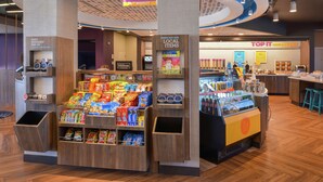 Zona comercial abierta las 24 horas, con opciones de comida y bebida, exhibición de productos locales y una sección de desayuno.