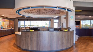 Un área de recepción moderna de hotel con un mostrador curvo, una estación de café y grandes ventanales con vistas al exterior.