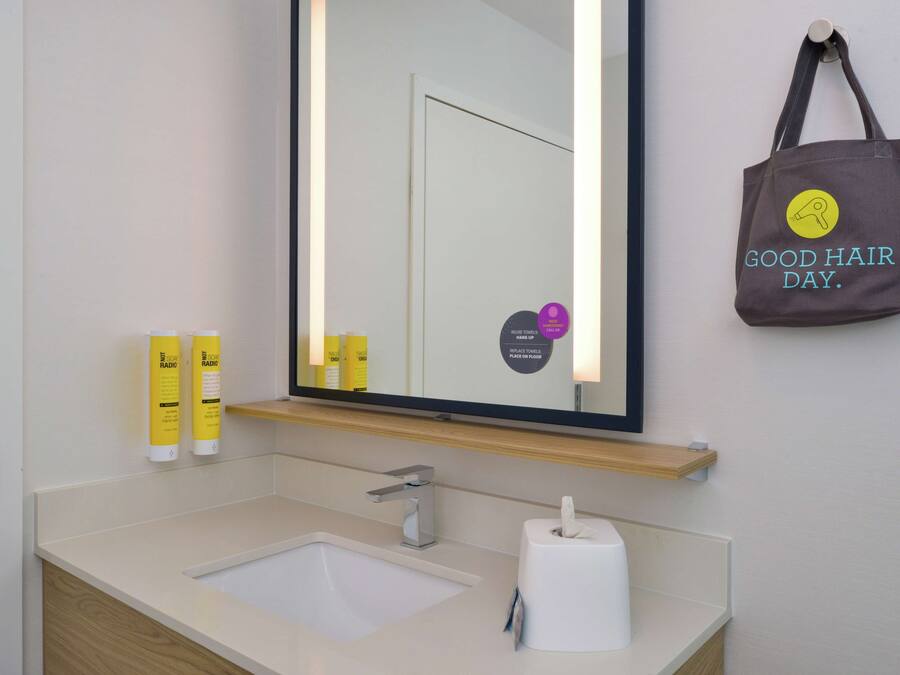 A bathroom with a sink, mirror, and a towel dispenser.