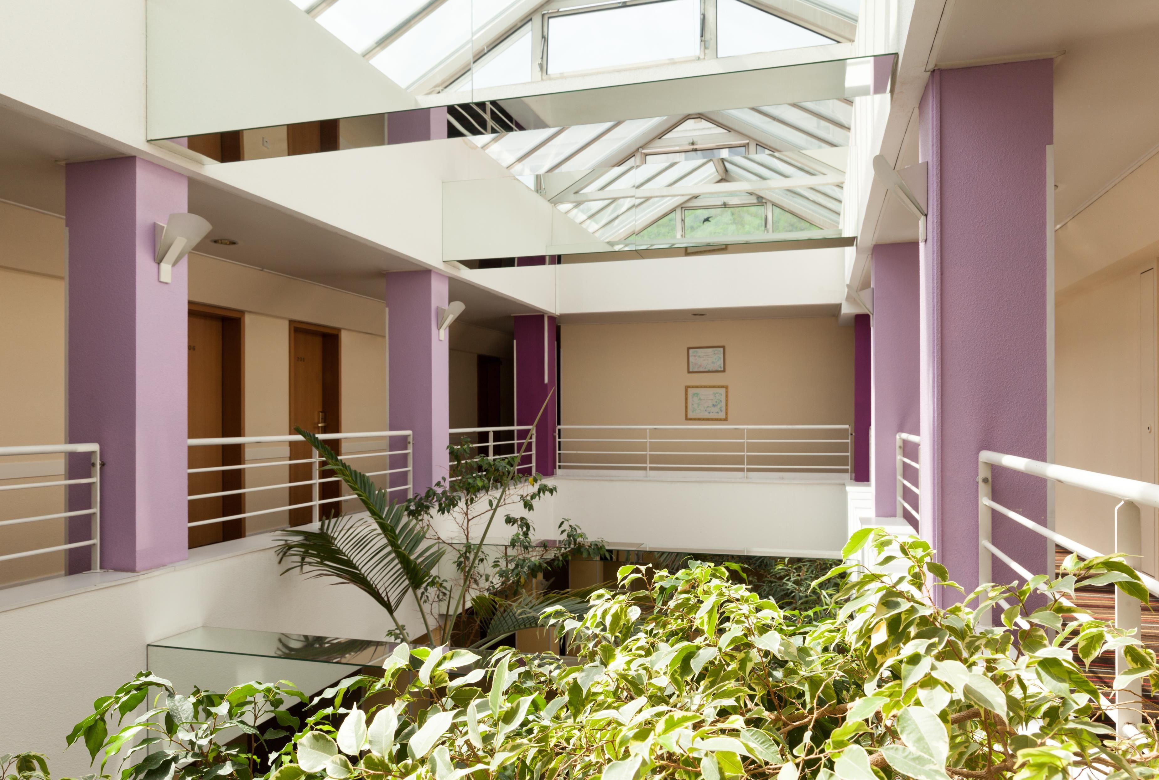 Un intérieur à plusieurs niveaux, doté de rampes en verre, d’un escalier central et de plantes d’intérieur.