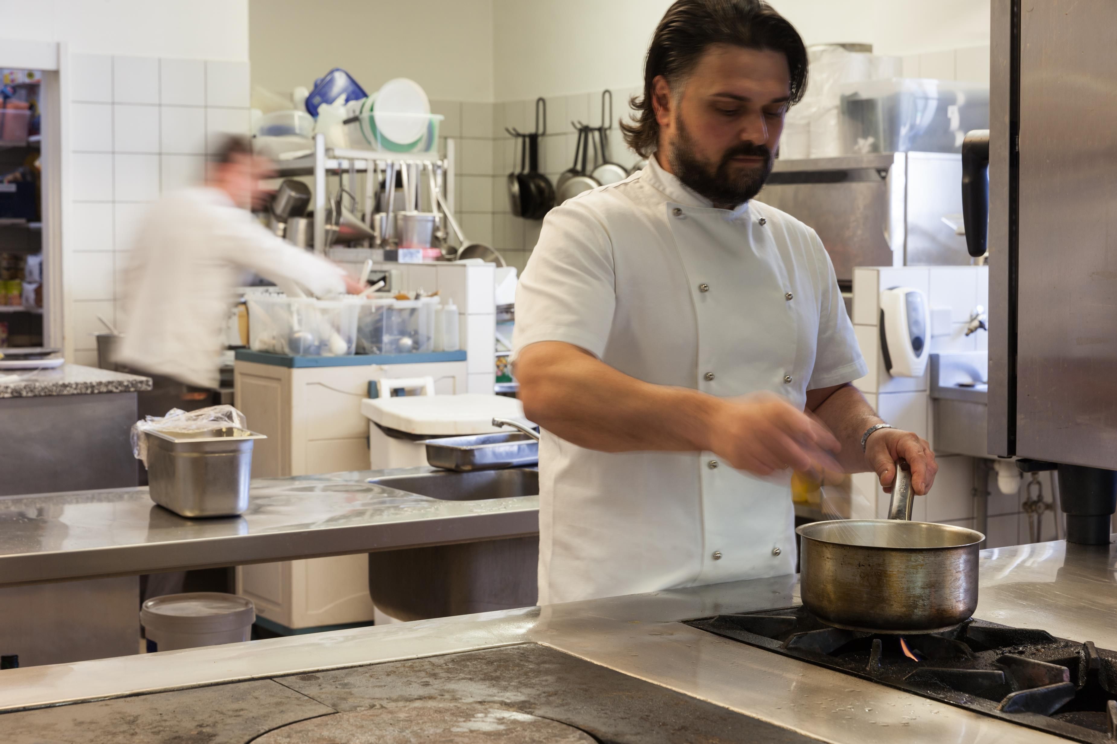 Un chef cocina en una cocina profesional con electrodomésticos y utensilios de acero inoxidable.