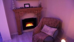 Habitació acollidora amb una llar de foc, un butac armchair rústic i una taula petita amb una espelma.