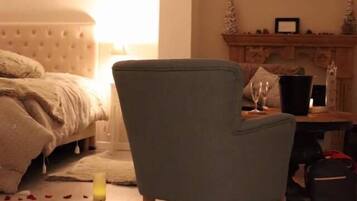 Un dormitorio con cama, una silla, una mesita de noche con una vela y pétalos de rosa en el suelo.