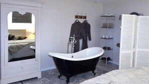 Un bany amb una banyera autònoma, un mirall i un lavabo blanc amb prestatges.