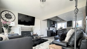 Una sala de estar moderna con chimenea, televisor de pantalla plana y comedor con cocina al fondo.