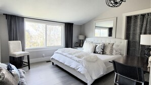 Un dormitorio moderno con una cama grande, una silla, un escritorio y un ventanal con cortinas.