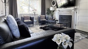 Una sala de estar con chimenea, televisor y sofá con almohadones decorativos.