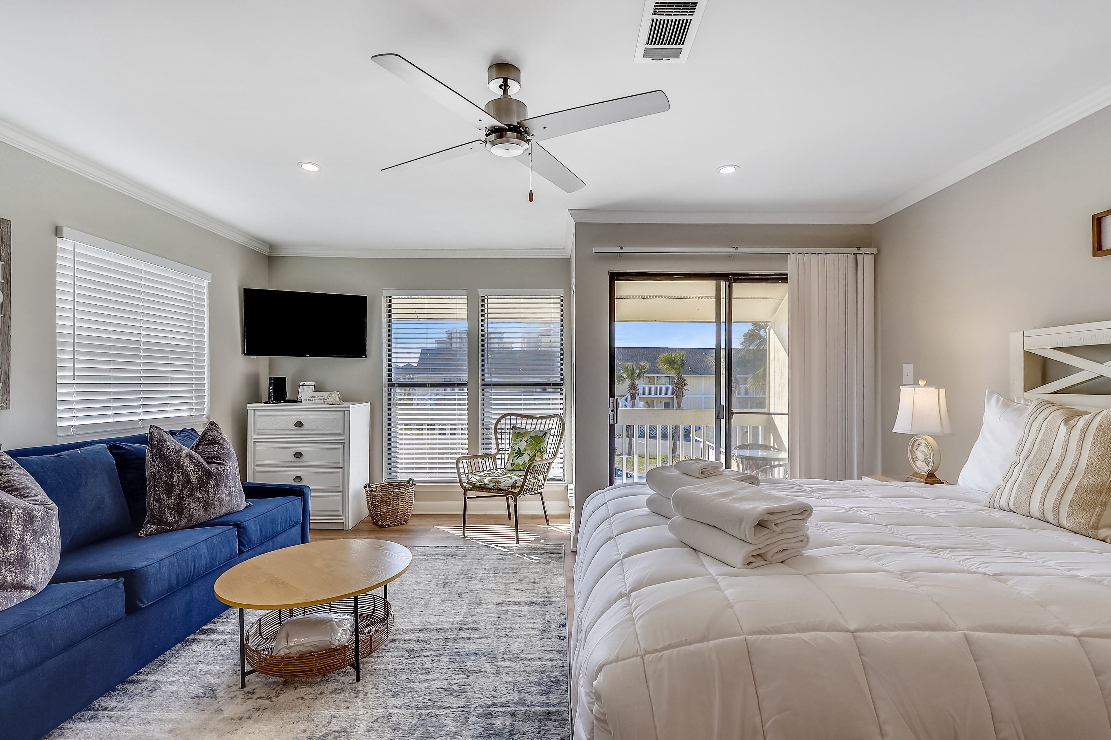 A modern bedroom with a large bed, a blue sofa, a TV, and a balcony with a view.