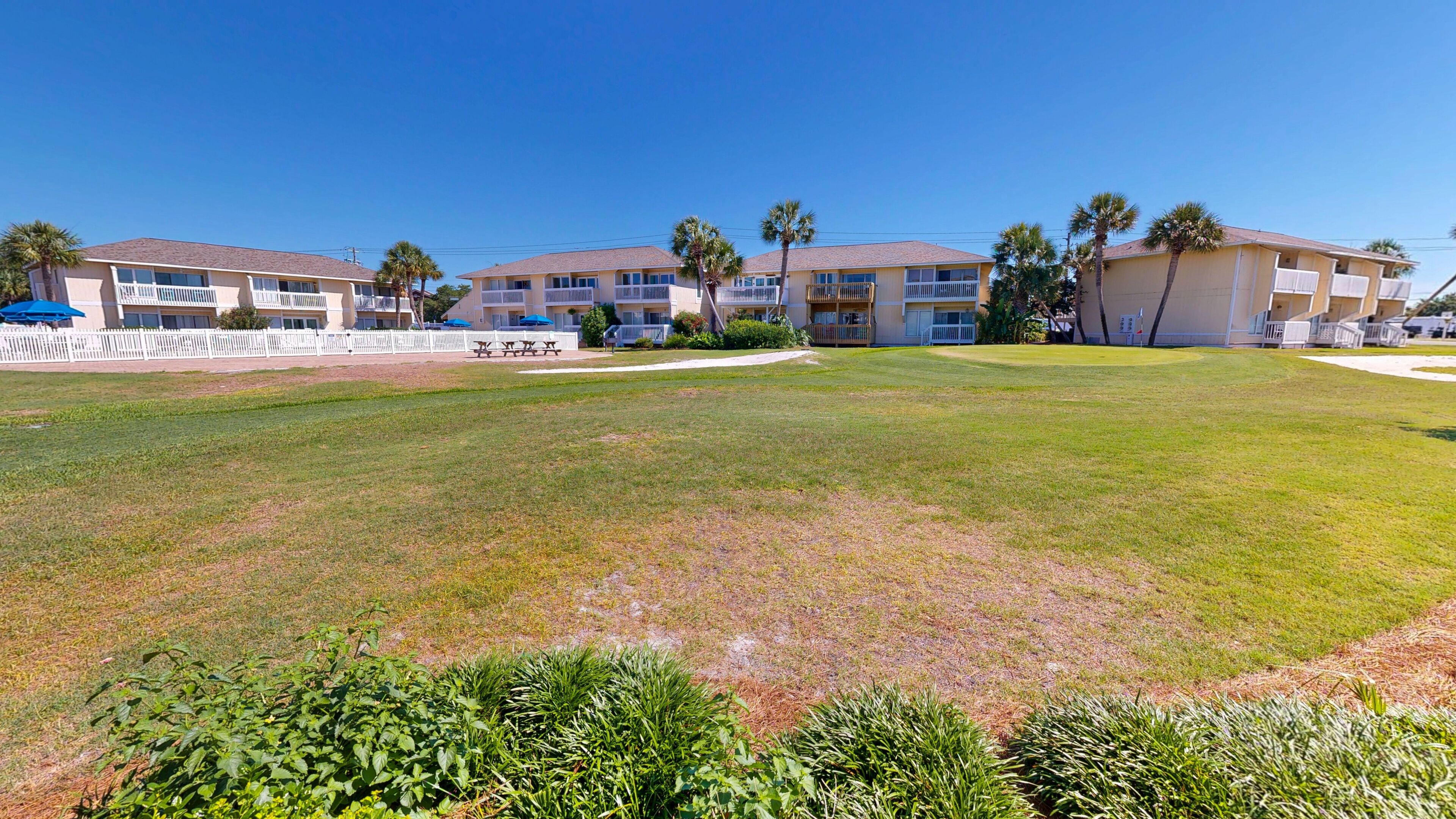 A hotel with multiple balconies, a grassy lawn, and palm trees.