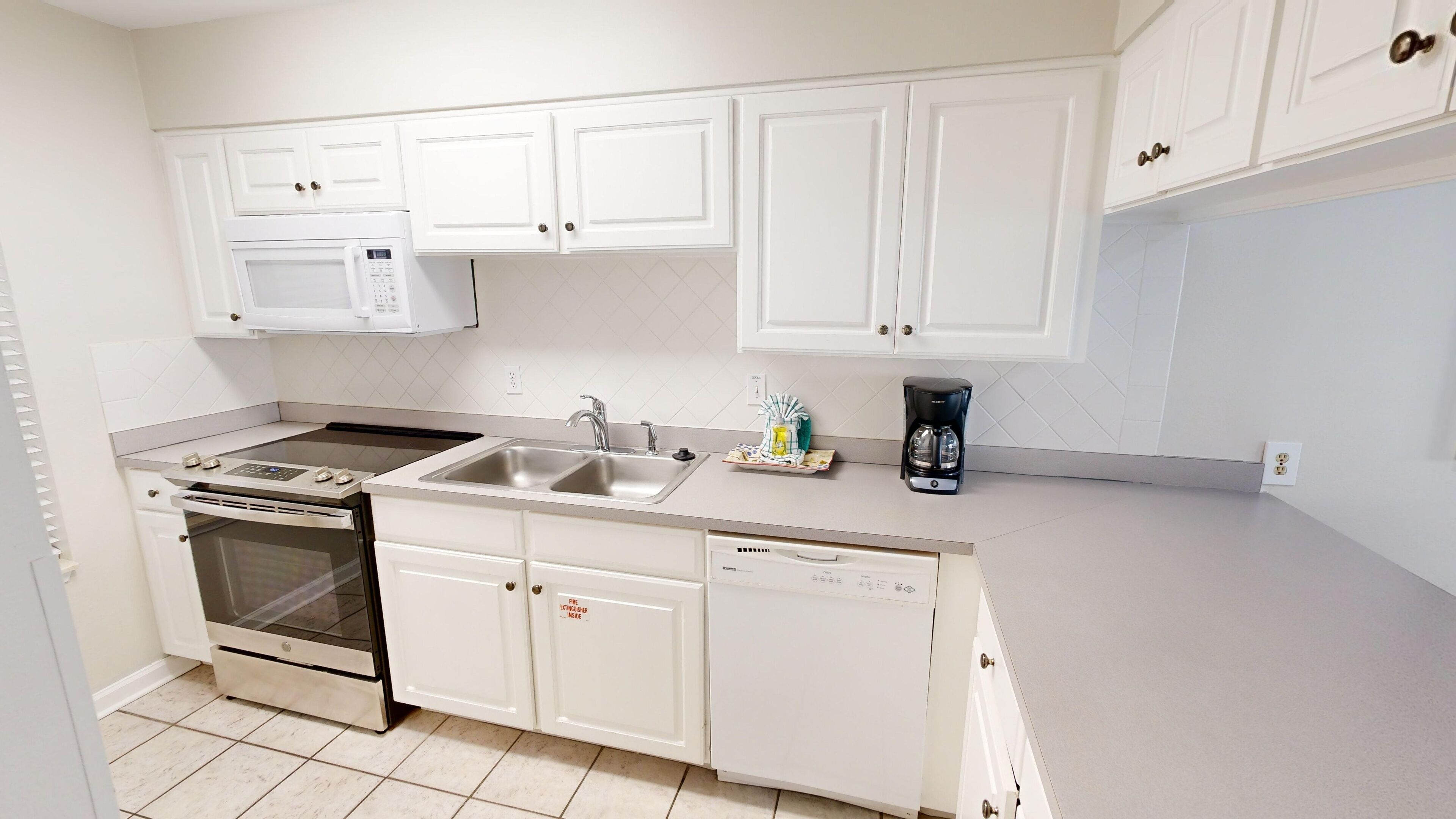 A modern kitchen with white cabinetry, a built-in microwave, a coffee maker, and a dishwasher.