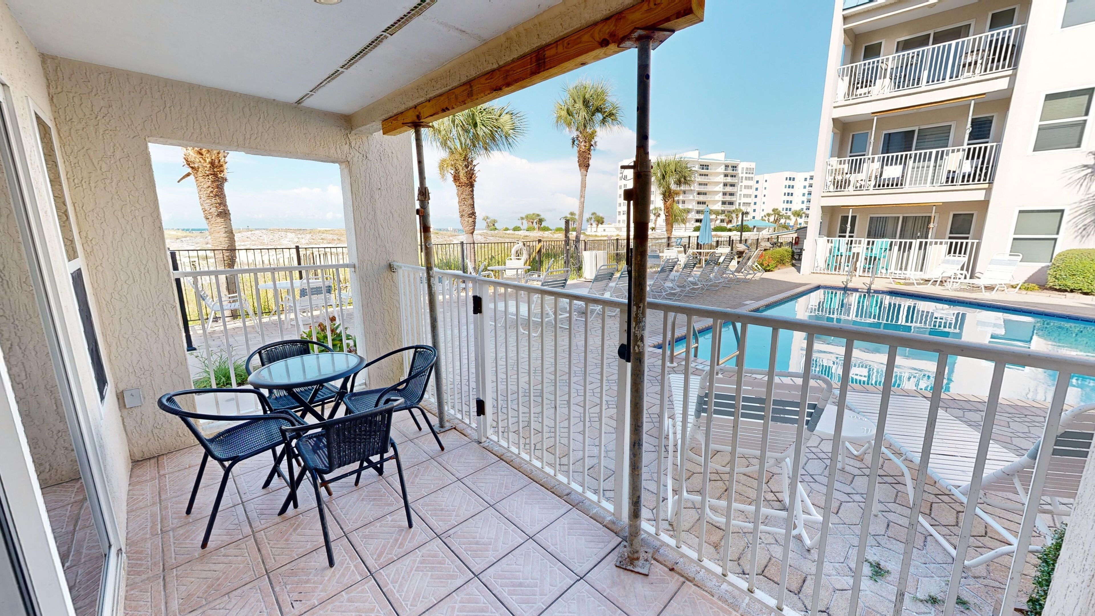 A balcony with a table and chairs, a pool, and palm trees.