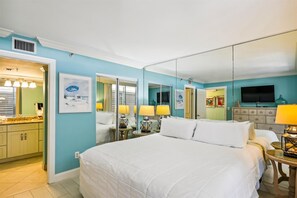 Una habitación de hotel con una cama grande, un baño con lavamanos y espejo, y un televisor.