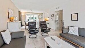 A modern living room with a sofa, two leather chairs, a coffee table, and a dining area in the background. - Campanula (Koksijde)