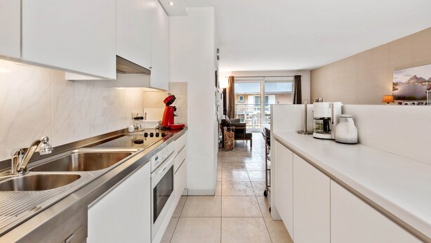 A modern kitchen with stainless steel appliances, white cabinetry, and a view to the living area. - Campanula (Koksijde)