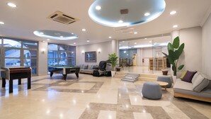 A spacious lobby with a pool table, seating area, and large windows. - Karras Grande Resort (Zakynthos)