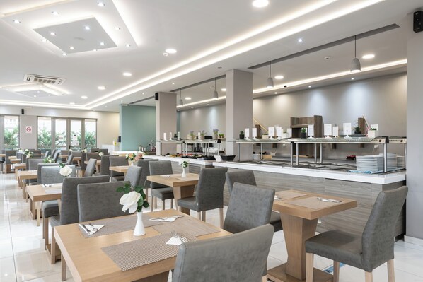A modern restaurant with a long counter, multiple tables, and chairs. - Karras Grande Resort (Zakynthos)