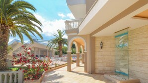 A hotel corridor with a palm tree, a glass wall with a sign, and a tiled floor. - Karras Grande Resort (Zakynthos)