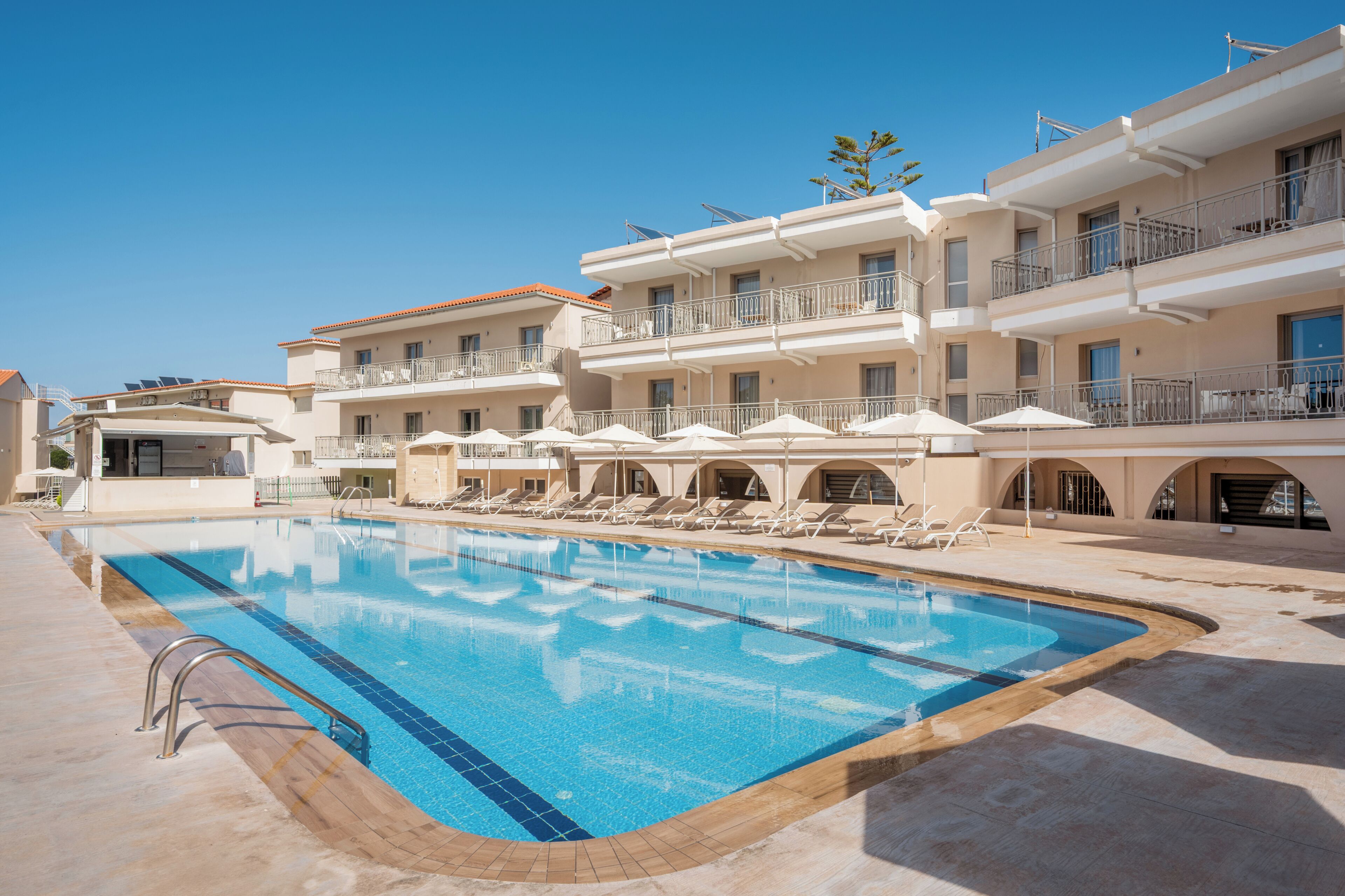 A swimming pool with sun loungers and umbrellas, surrounded by multi-story buildings with balconies.