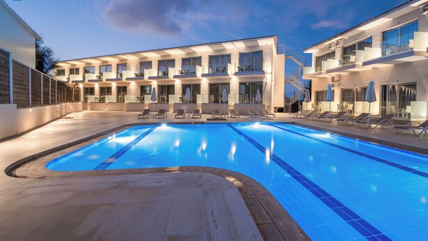 A swimming pool with lounge chairs, a covered seating area, and a building with multiple balconies. - Karras Grande Resort (Zakynthos)
