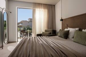 Habitación de hotel con una cama grande, una silla, una mesa y un balcón con vistas a edificios.