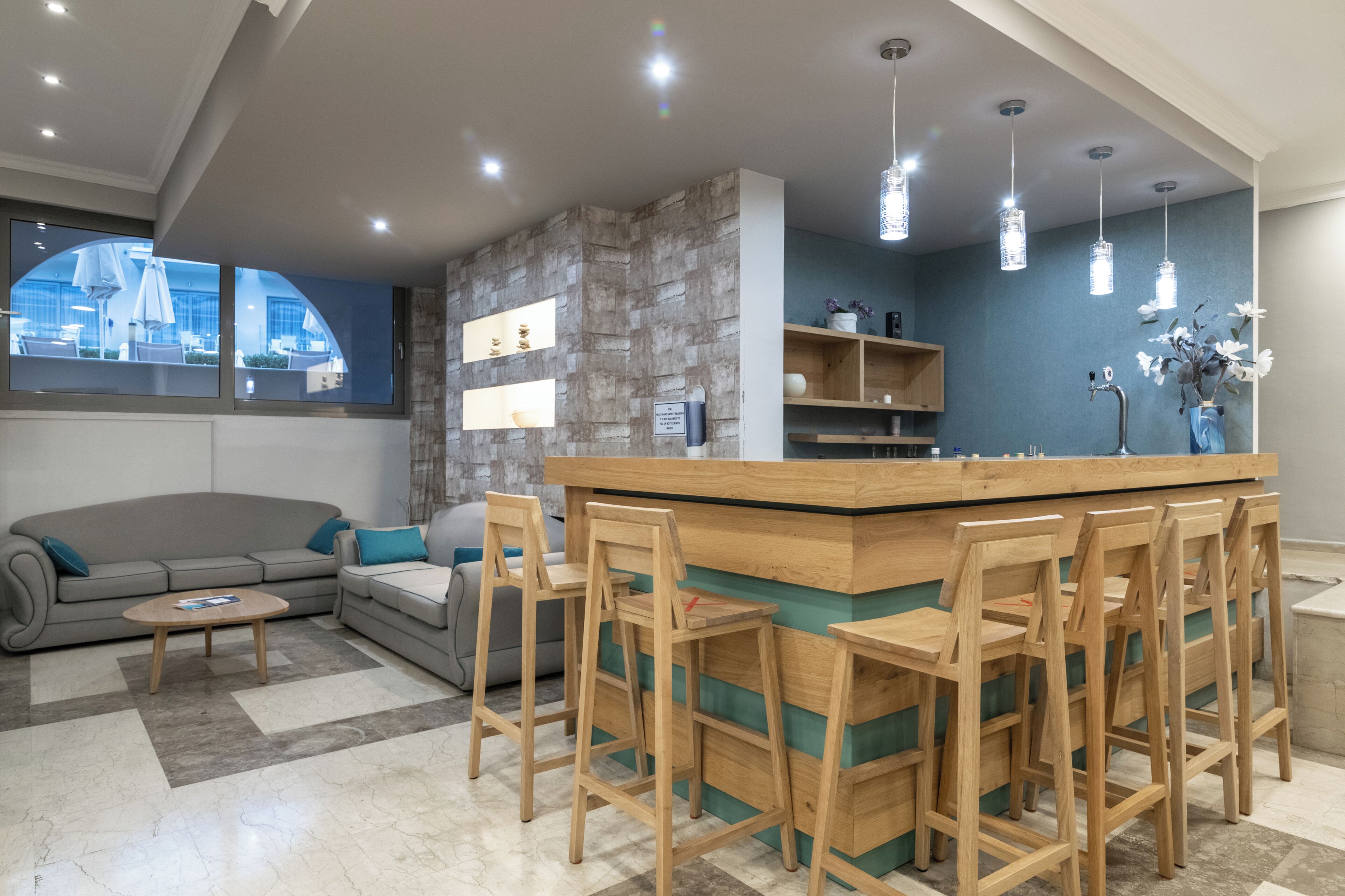 Un salon moderne comprenant un canapé, une table basse, un bar en bois avec des tabourets et un mur d’accent en pierre.
