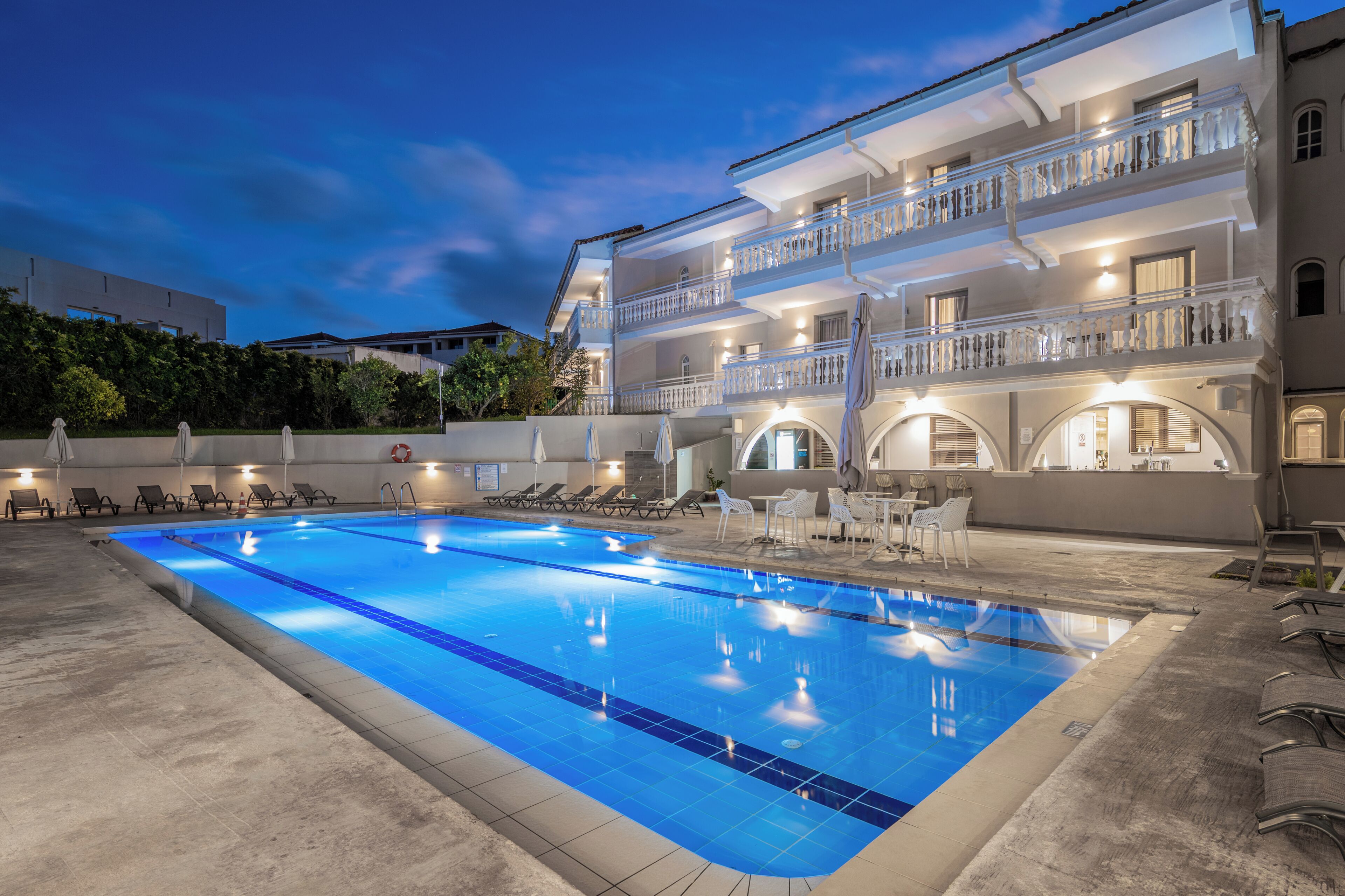 A swimming pool with lounge chairs and a building with balconies.
