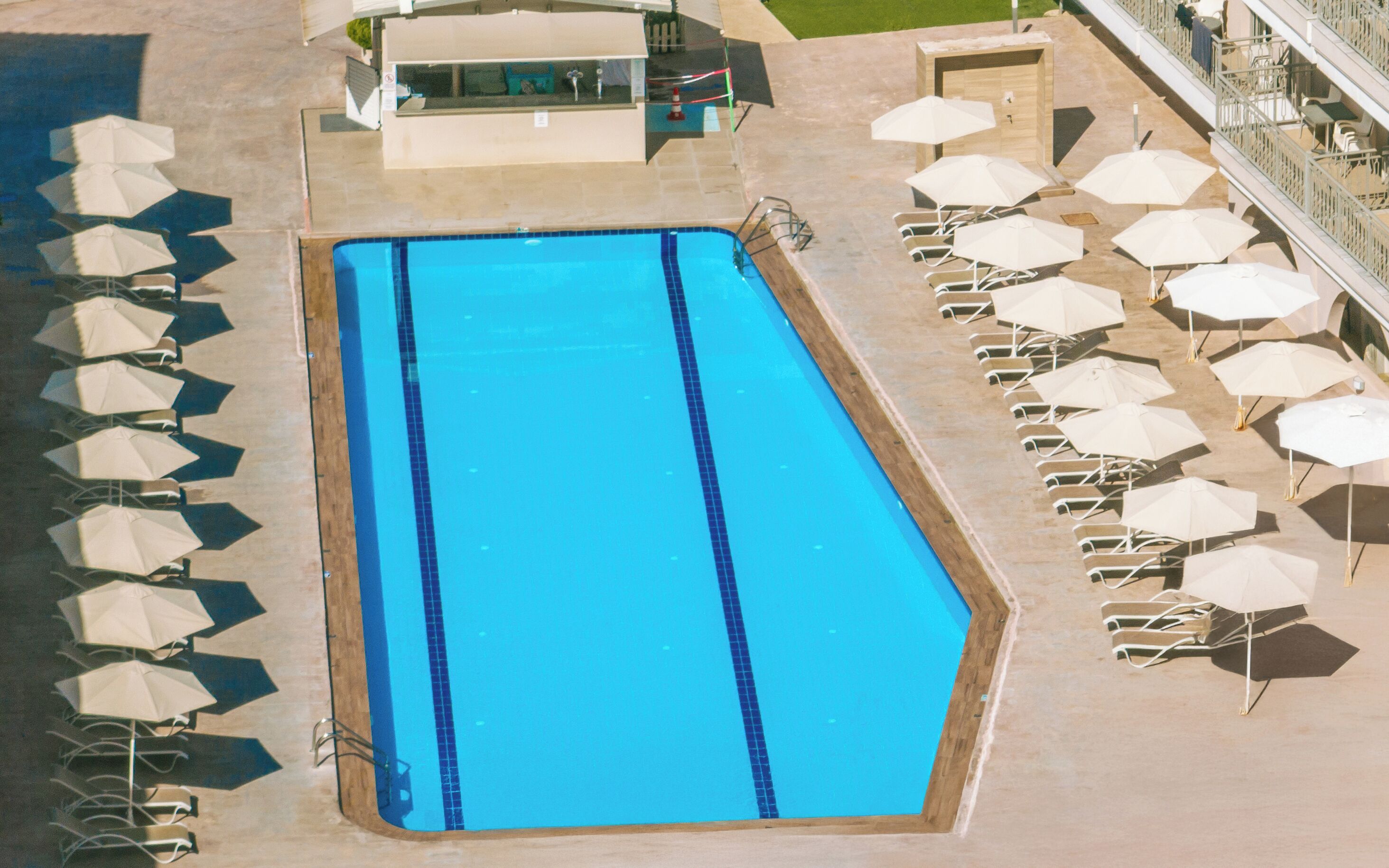 Una piscina rectangular con borde de azulejos, rodeada de sillas de descanso y sombrillas.