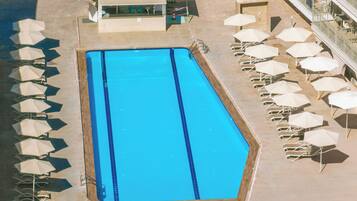 Una piscina rectangular con borde de azulejos, rodeada de sillas de descanso y sombrillas.