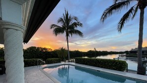 Una piscina con vistas a una puesta de sol sobre el agua, rodeada de palmeras y un muelle.