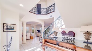 Un piano de cola imponente en una habitación amplia y luminosa, con techo alto y una escalera decorativa.