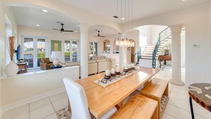 Un amplio espacio de sala con una larga mesa de comedor de madera, sofás blancos y una escalera que conduce a un piso superior.