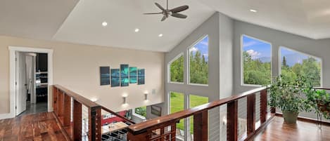A spacious interior with a wooden staircase, large windows, and a ceiling fan.