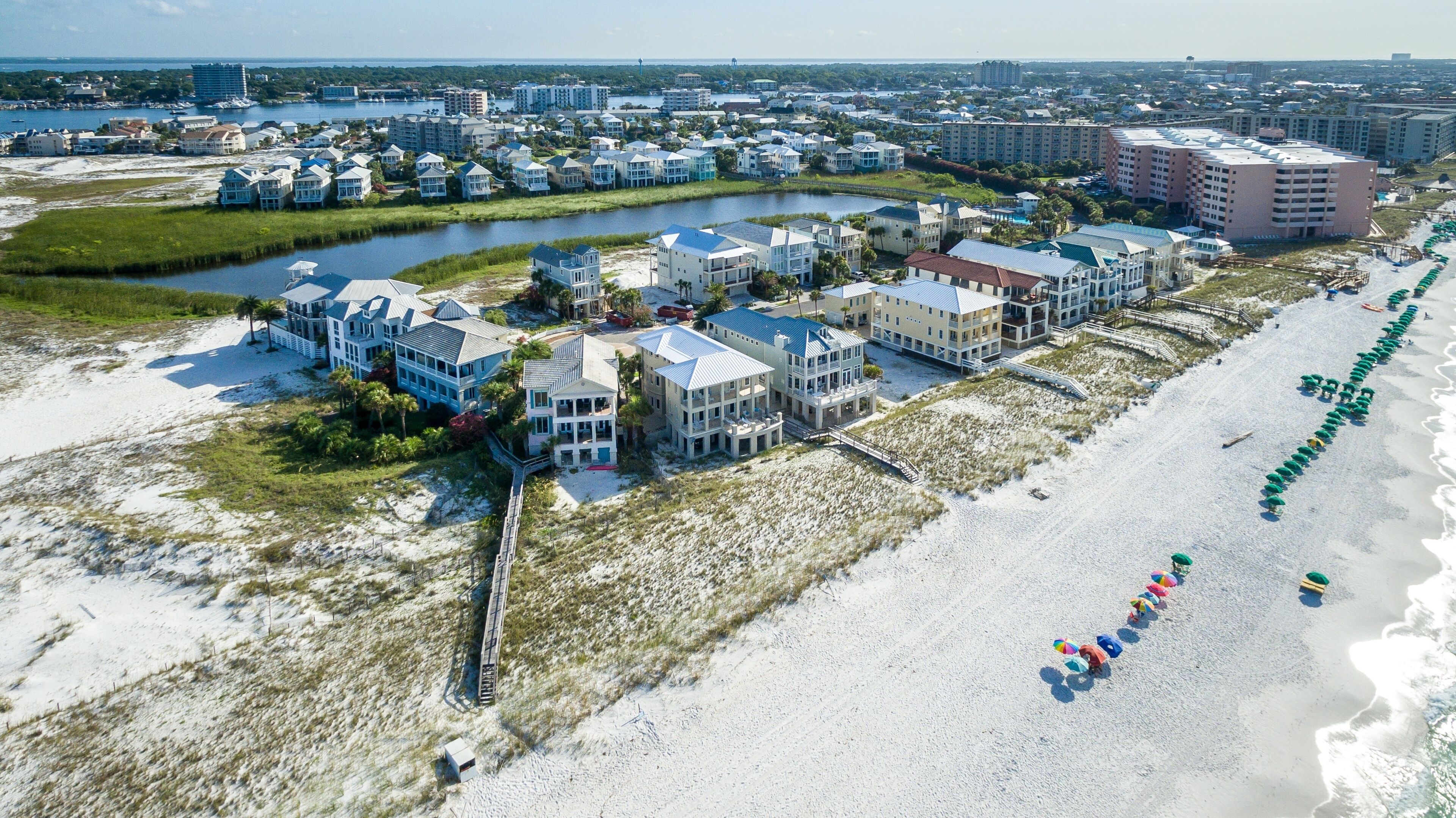 An aerial view of a coastal resort with beachfront properties, a marina, and a long stretch of beach with umbrellas.