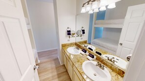 Ein Badezimmer mit zwei Waschbecken, einem großen Spiegel und einem Stockbett im Hintergrund.