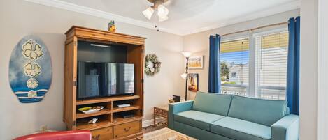 A living room with a teal sofa, a red armchair, a wooden entertainment center, and a ceiling fan.