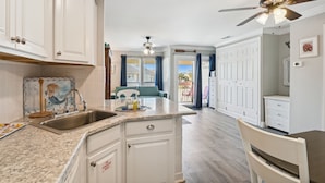 A kitchen with white cabinets, a granite countertop, and a ceiling fan. - Sandpiper Cove 8245 Studio Bedroom Condo by RedAwning (Destin)
