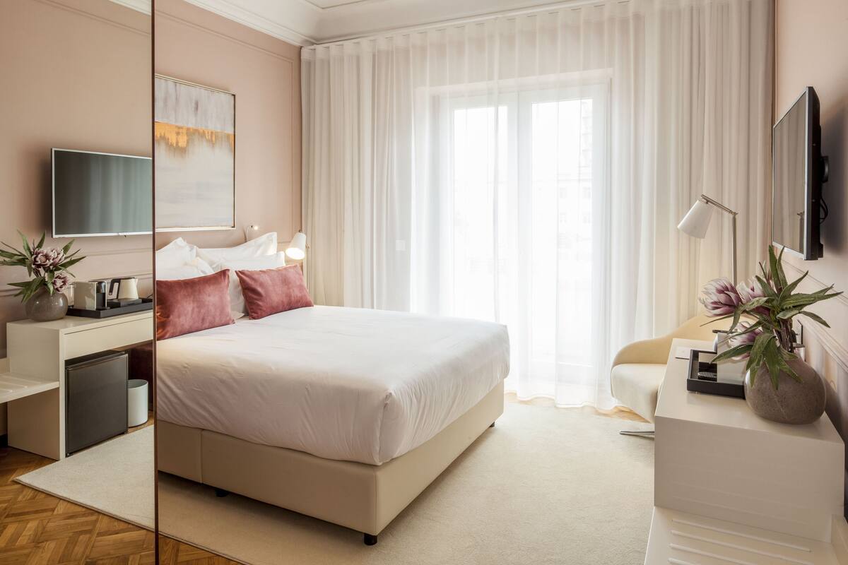 A modern hotel room with a large bed, a flat-screen TV, a desk with a lamp, and a potted plant.
