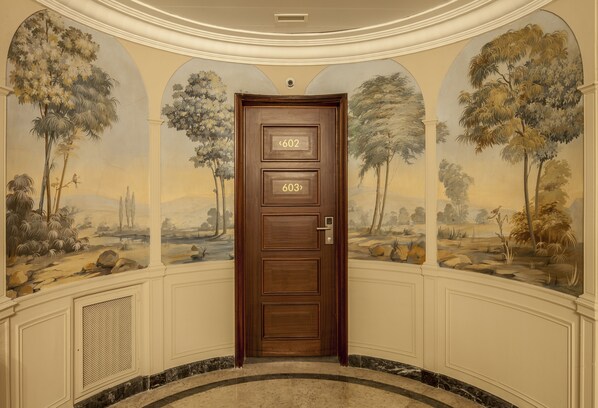 Puerta de madera con los números 602 y 603, ubicada en un pasillo con un mural de árboles y paisajes.