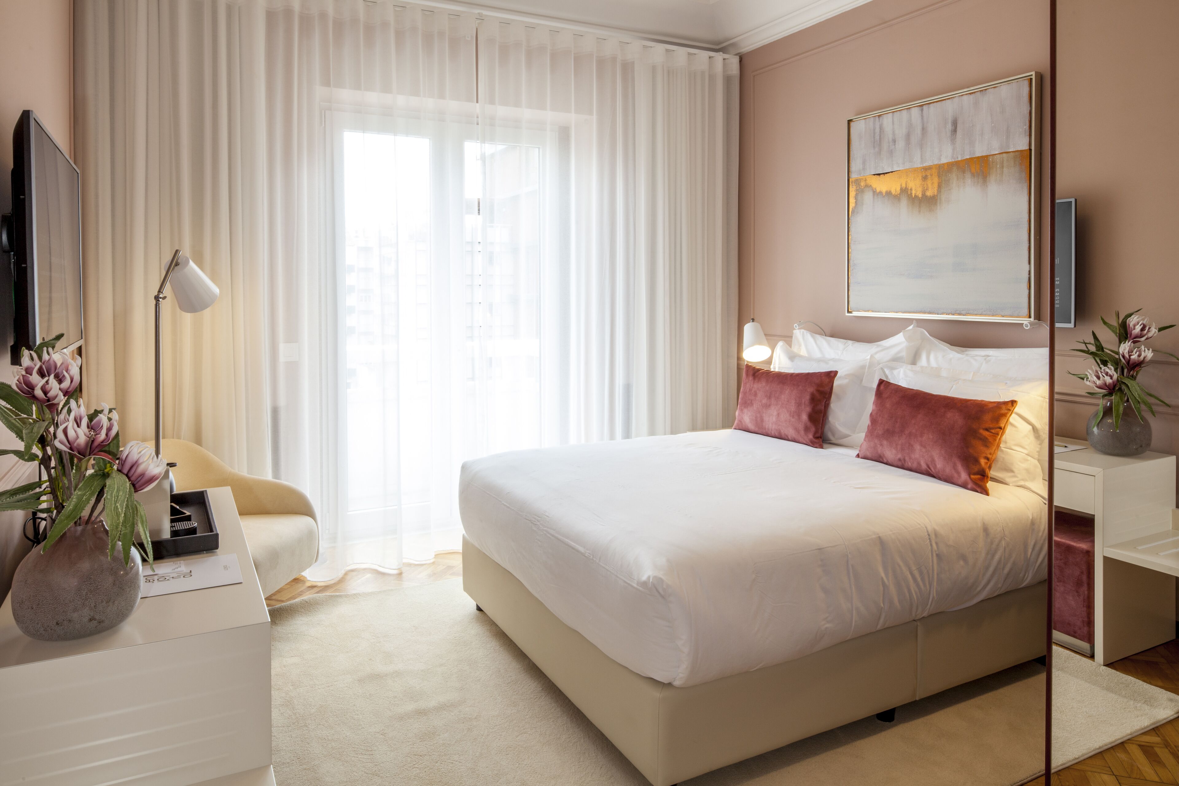 A modern bedroom with a large bed, a bedside table, a lamp, and a painting on the wall.