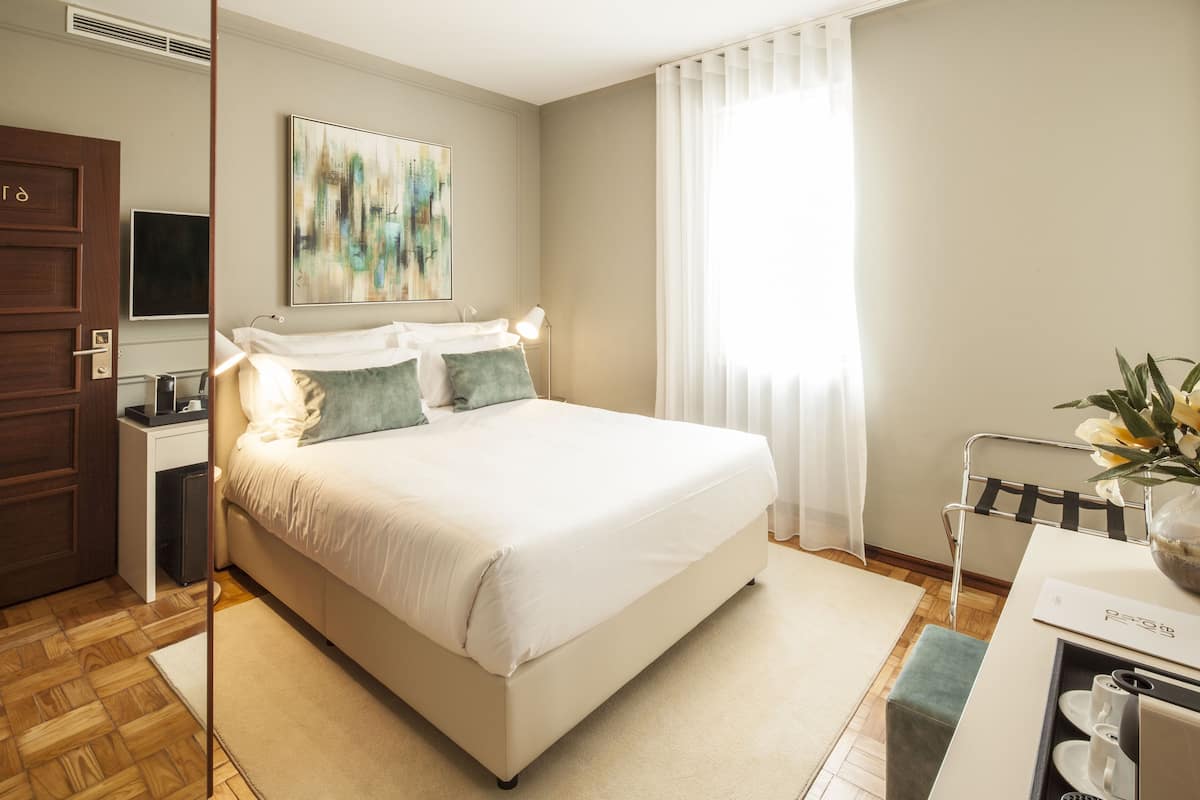 A modern hotel room with a large bed, bedside tables, a desk with a chair, a flat-screen TV, and a large abstract painting on the wall.