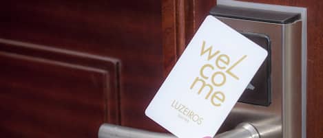 A hand holding a card with "Welcome" and "Luzieros Suites" written on it, inserted into a door lock.