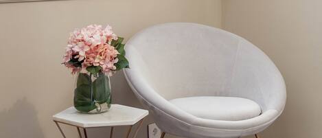 A white chair next to a small white table with a vase of pink flowers.