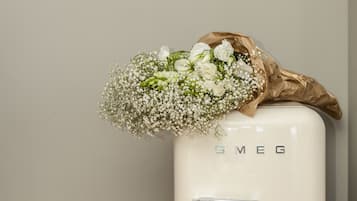 A vintage white refrigerator with the brand name 'SMEG' on it, placed against a plain wall with a thermostat and a welcome card visible.