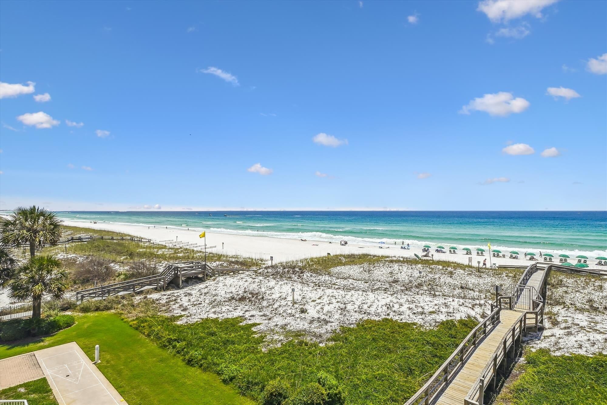 A beach with a wooden boardwalk leading to the shore, clear blue sky, and calm sea.