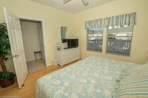 Ein Schlafzimmer mit Bett, Schminktisch, Fernseher, Spiegel und einem Fenster mit Jalousien.