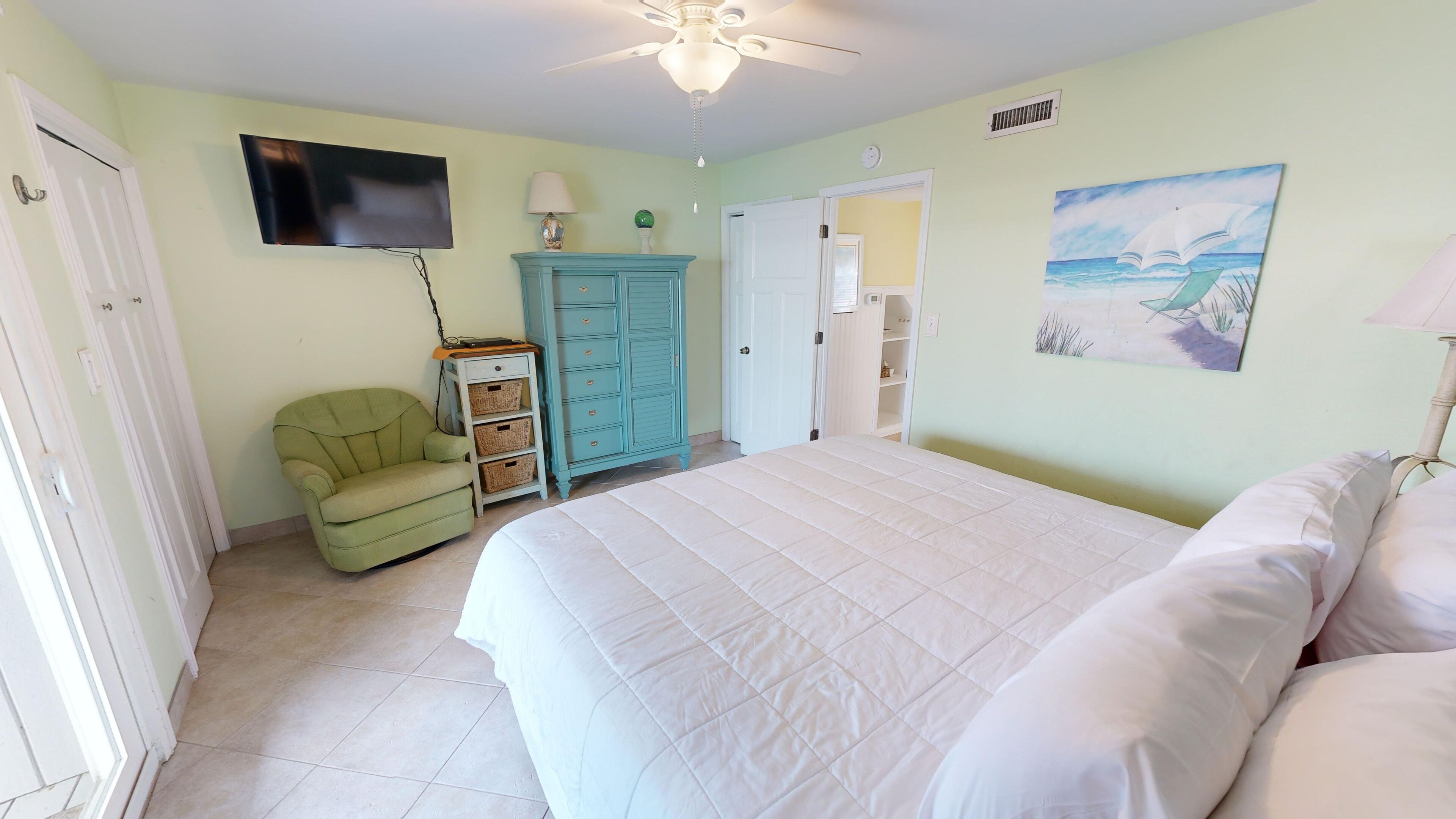 A bedroom with a bed, a chair, a wardrobe, a television, and a painting on the wall.
