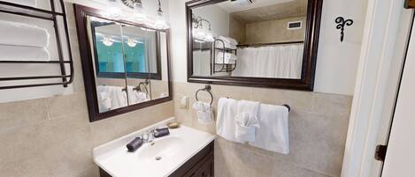 A bathroom with a white sink, two mirrors, and a towel rack with multiple towels.