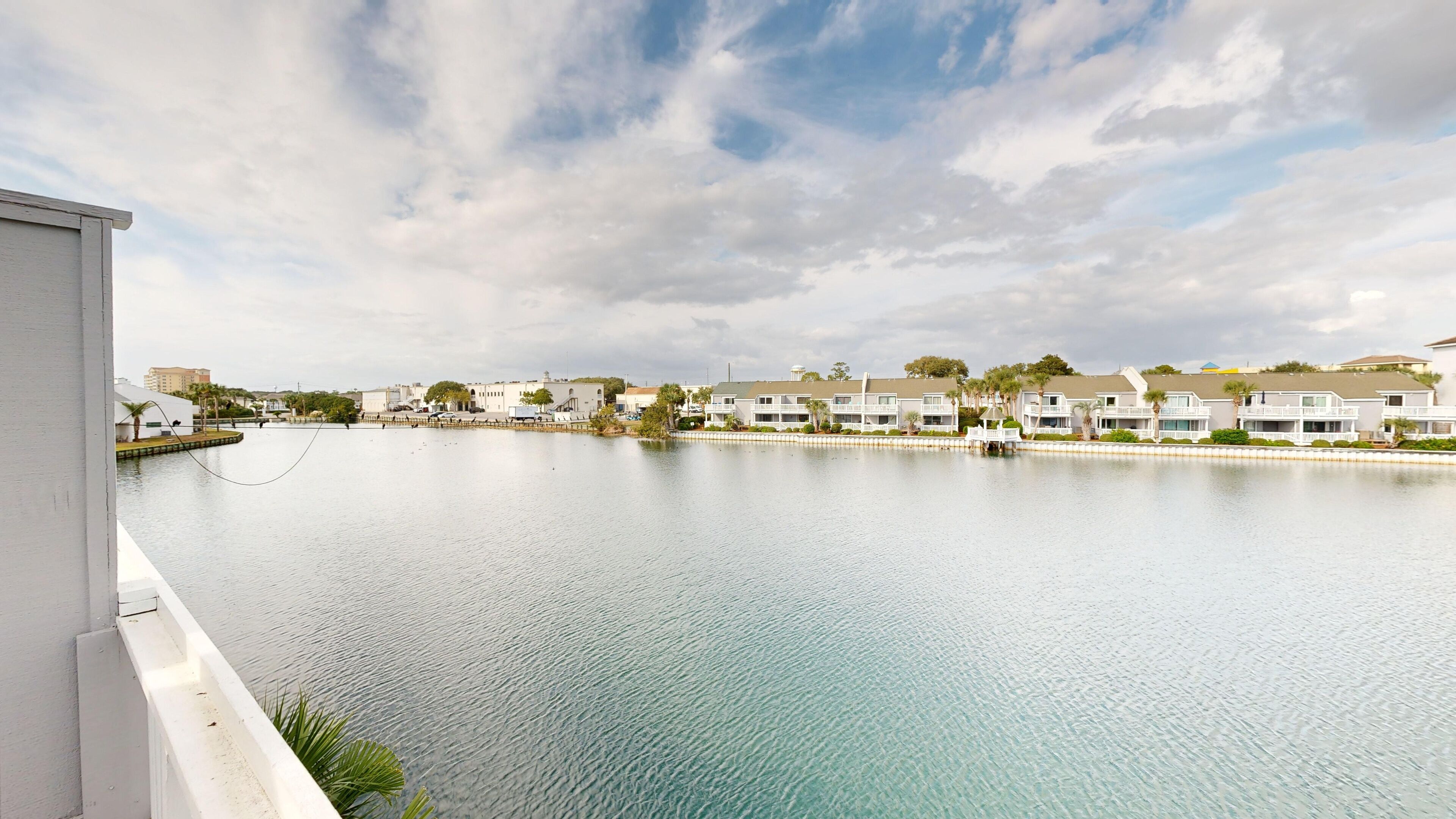 A waterfront view with a row of white buildings, a calm body of water, and a clear sky.