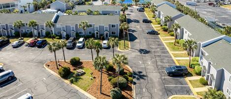 A multi-story residential building with a parking lot, palm trees, and a view of the ocean.